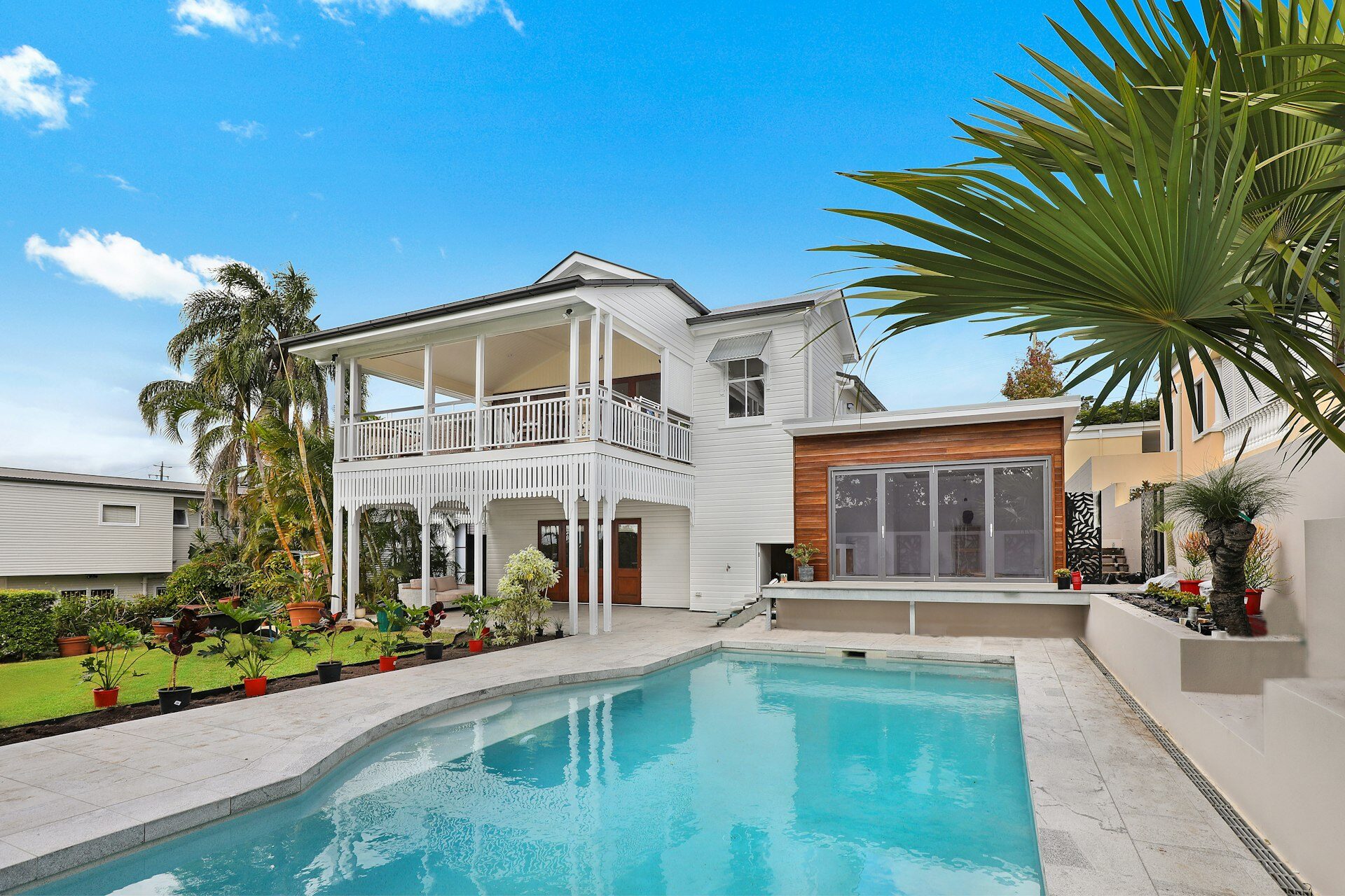 Modern two-storey residential home with swimming pool and landscaped garden under blue sky